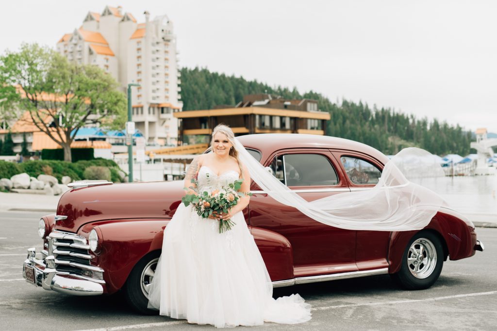 _A1S8923-2 Bride photography with veil flying in front of maroon vintage car in coeur d'alene ID